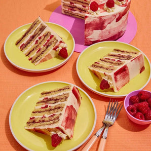 Raspberry Ripple Cake with eight layers of raspberry sponge, whipped vanilla icing, fresh raspberries, and raspberry decoration.